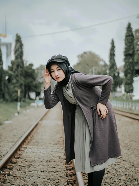 a woman standing on a train track wearing a hijab, unsplash, hurufiyya, in gunmetal grey, short skirt and a long jacket, unreal ungine 5, portrait mode photo