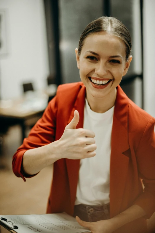 a woman sitting in front of a laptop giving a thumbs up, by Emma Andijewska, pexels contest winner, wearing red formal attire, wearing a fancy jacket, wearing business casual dress, smiley