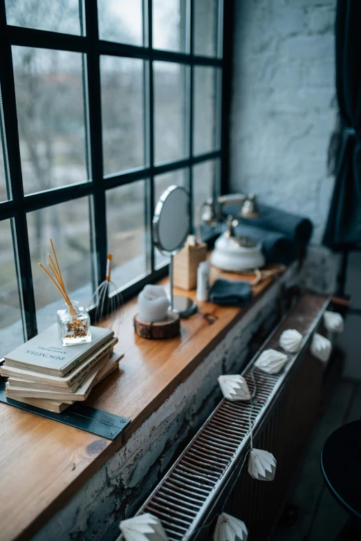 a wooden table topped with books next to a window, inspired by Elsa Bleda, pexels contest winner, with a mirror, industrial aesthetic, miniature porcelain model, winter