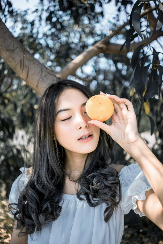 a woman holding an orange up to her eye, a picture, by helen huang, trending on pexels, sexy sesame seed buns, kuntilanak on tree, ulzzang, icon