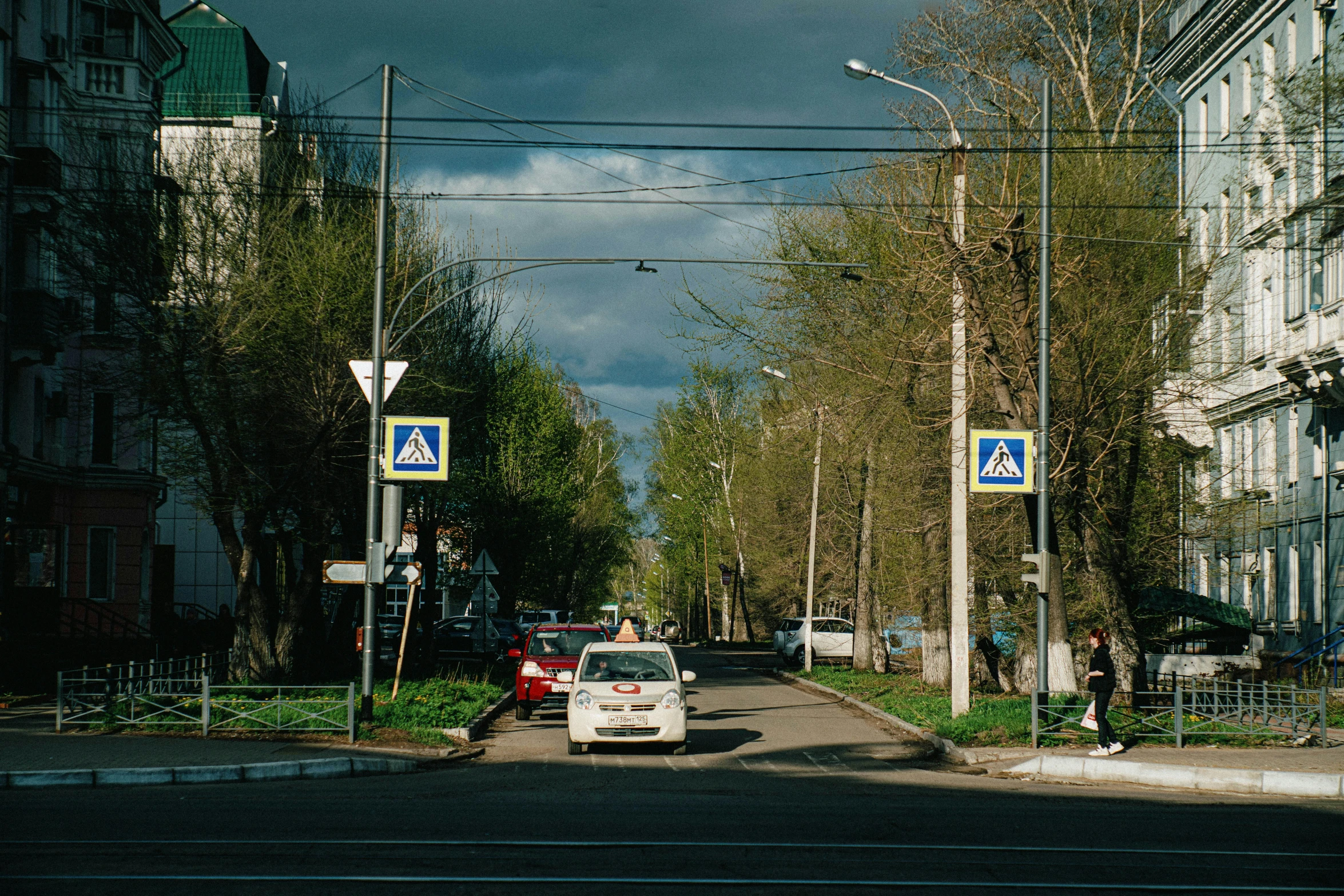 a white car driving down a street next to tall buildings, by Alexander Runciman, unsplash, realism, pripyat, gas street lamps. country road, nice spring afternoon lighting, people waiting in bus stop