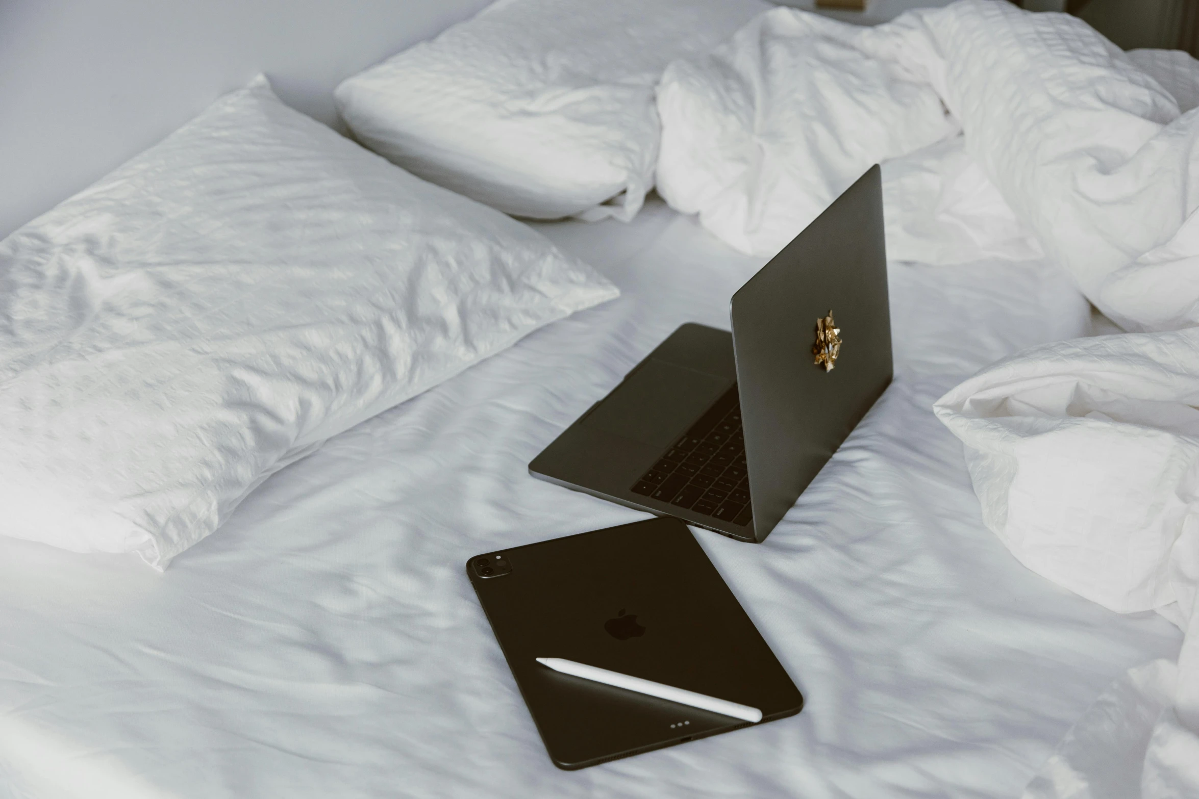 two laptops sitting on a white bed with blankets on it