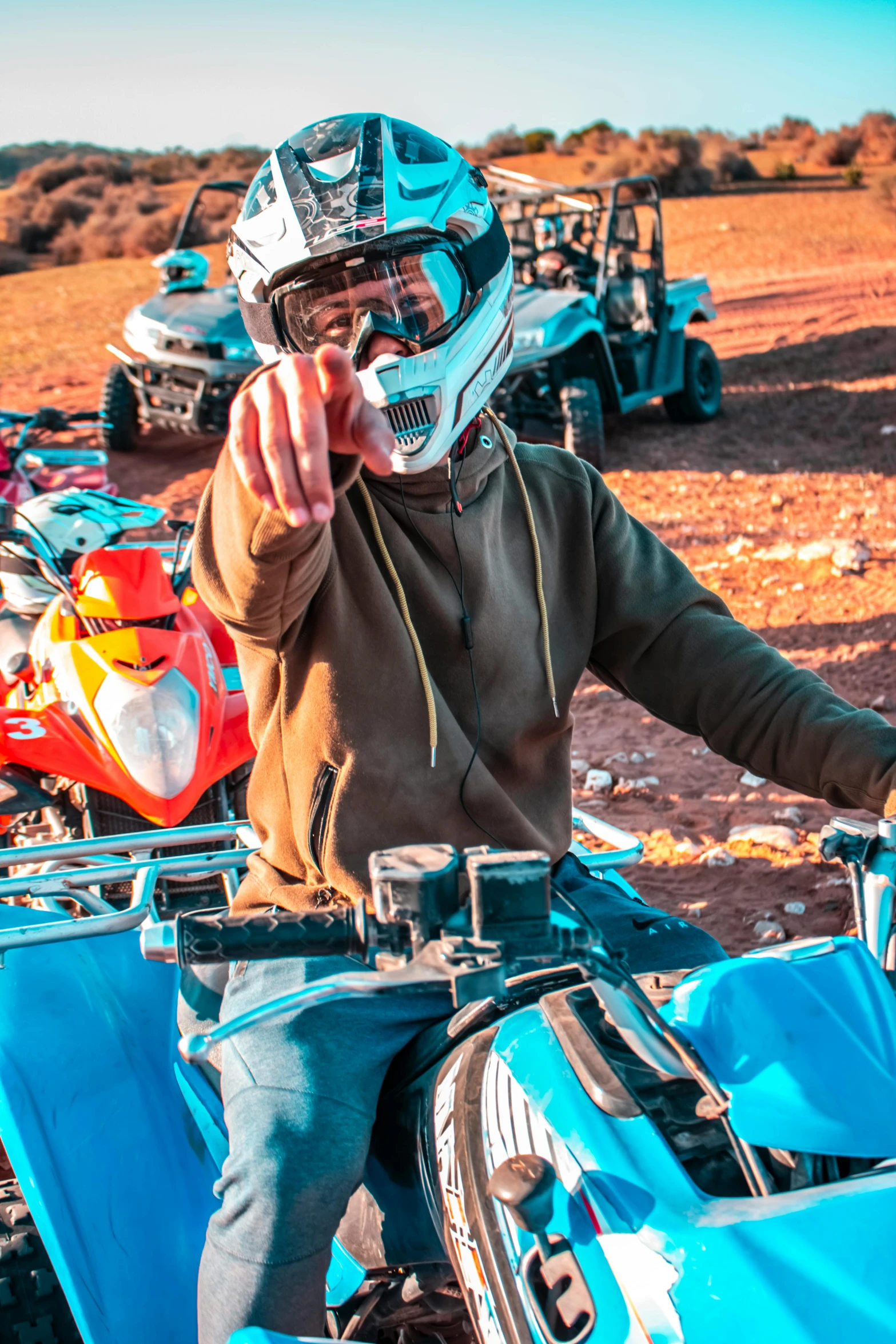 a man riding on the back of a blue motorcycle, pointing at the camera, outback, wearing adventure gear, center of image