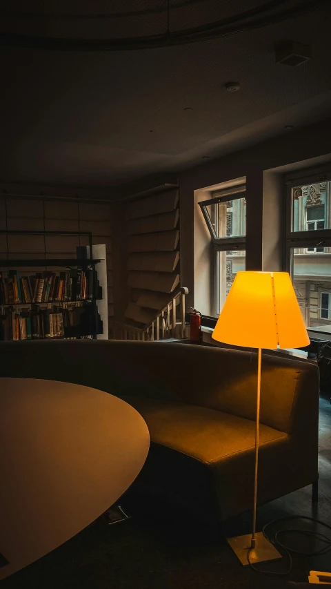 a lamp sitting on top of a table next to a couch, by Sebastian Spreng, unsplash contest winner, small library, yellow light, slanted lighting from window, soft light - n 9