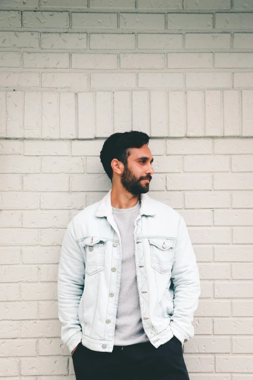 a man standing against a brick wall wearing a white jacket