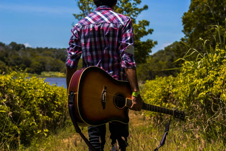 a man standing in a field holding a guitar, pexels contest winner, gazing at the water, sydney park, country style, mohamed chahin style