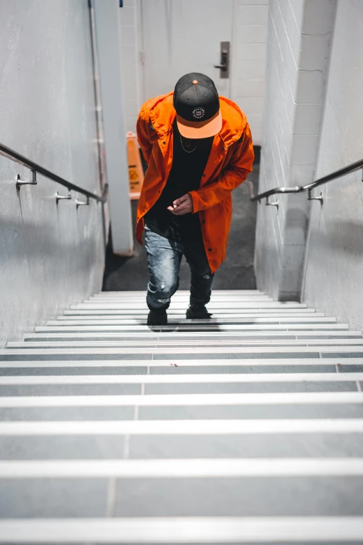 a man walking down a flight of stairs, pexels contest winner, happening, orange hoodie, baggy clothing and hat, ( ( theatrical ) ), virgil abloh