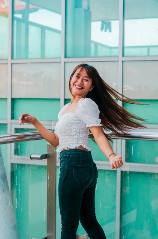 a woman with long hair standing in front of a building, inspired by helen huang, happening, smiling and dancing, wearing a cropped top, white and teal garment, standing on a bridge