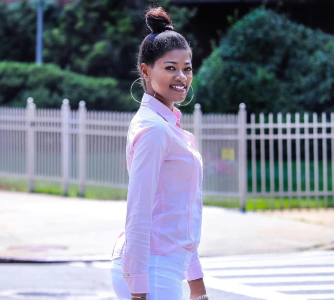 a woman in a pink shirt and white pants crossing a street, profile pic, nivanh chanthara, topknot, smiling