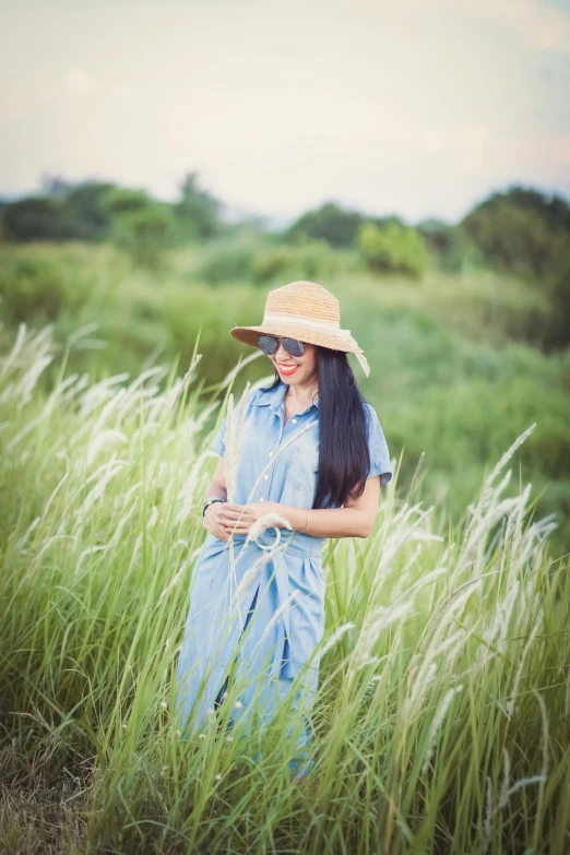 a woman wearing a blue dress and a straw hat is in tall grass