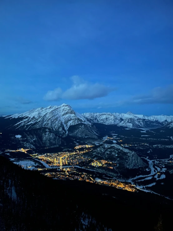 the view of snow capped mountains and city lights in the distance