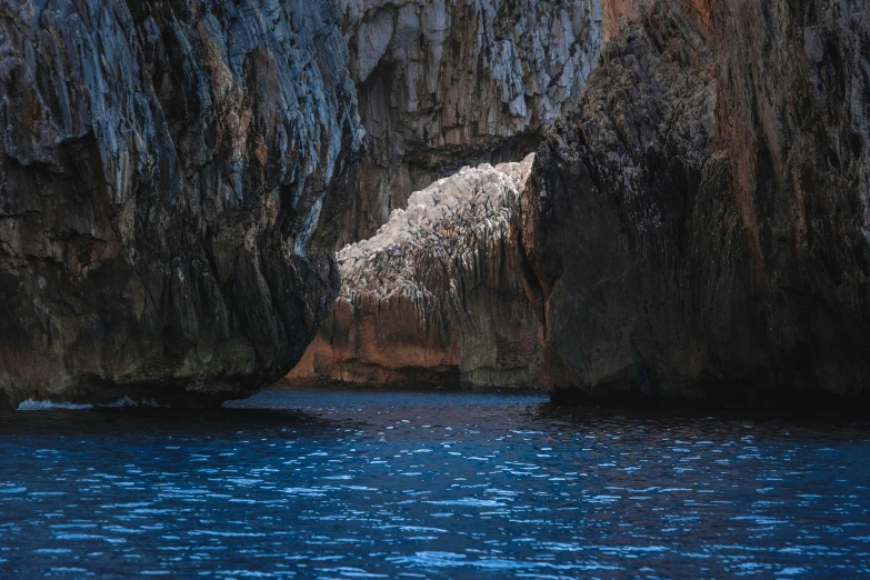 a large rock formation in the middle of a body of water, by Giuseppe Avanzi, pexels contest winner, romanticism, dark blue water, grotto, thumbnail, subtle detailing