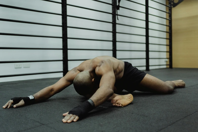 a man laying on the ground in a gym, by Matija Jama, hurufiyya, bending over, profile image, black spandex, lachlan bailey