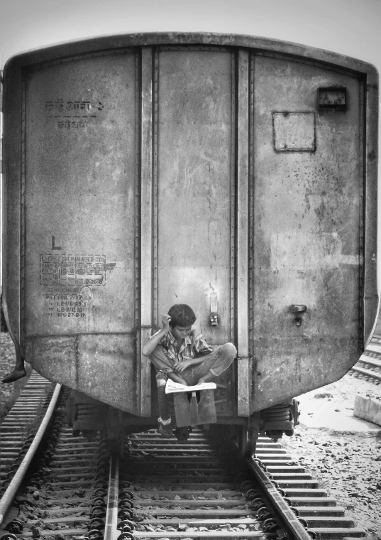 a black and white photo of a man sitting on a train, by Sudip Roy, conceptual art, trying to read, childhood, square, boy