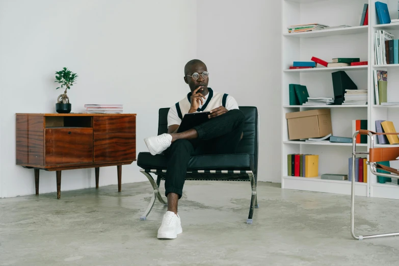 a man sitting in a chair talking on a cell phone, inspired by David Bailly, pexels contest winner, afrofuturism, minimalist home office, grey pants and black dress shoes, librarian, young thug