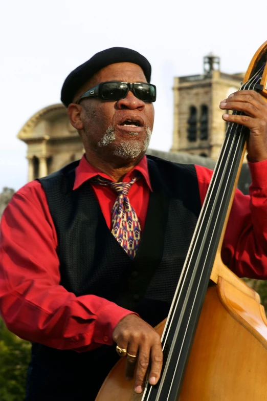 a man in a red shirt and black vest playing a double bass, morgan freeman, red sunglasses and a guitar