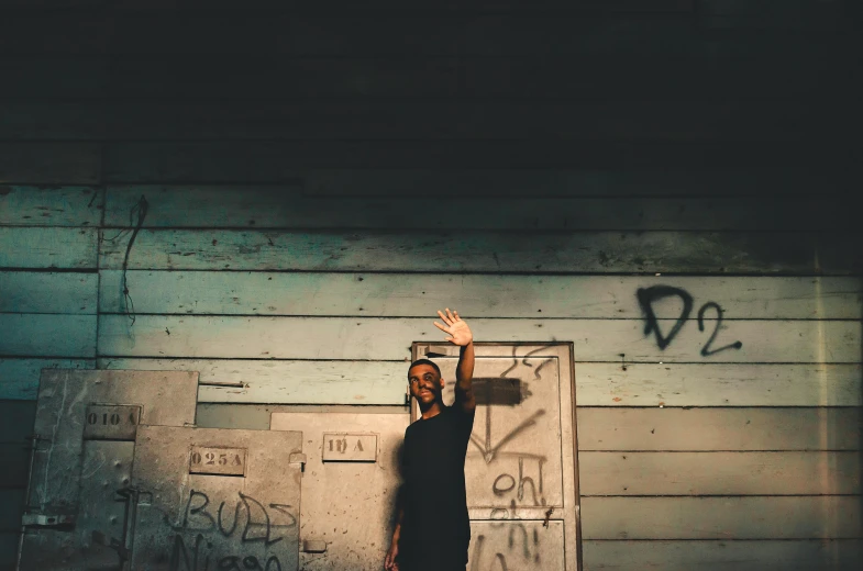 a man standing in front of a wall with graffiti on it, an album cover, by Lucia Peka, pexels contest winner, with arms up, dark moody, photo of a black woman, boarded up