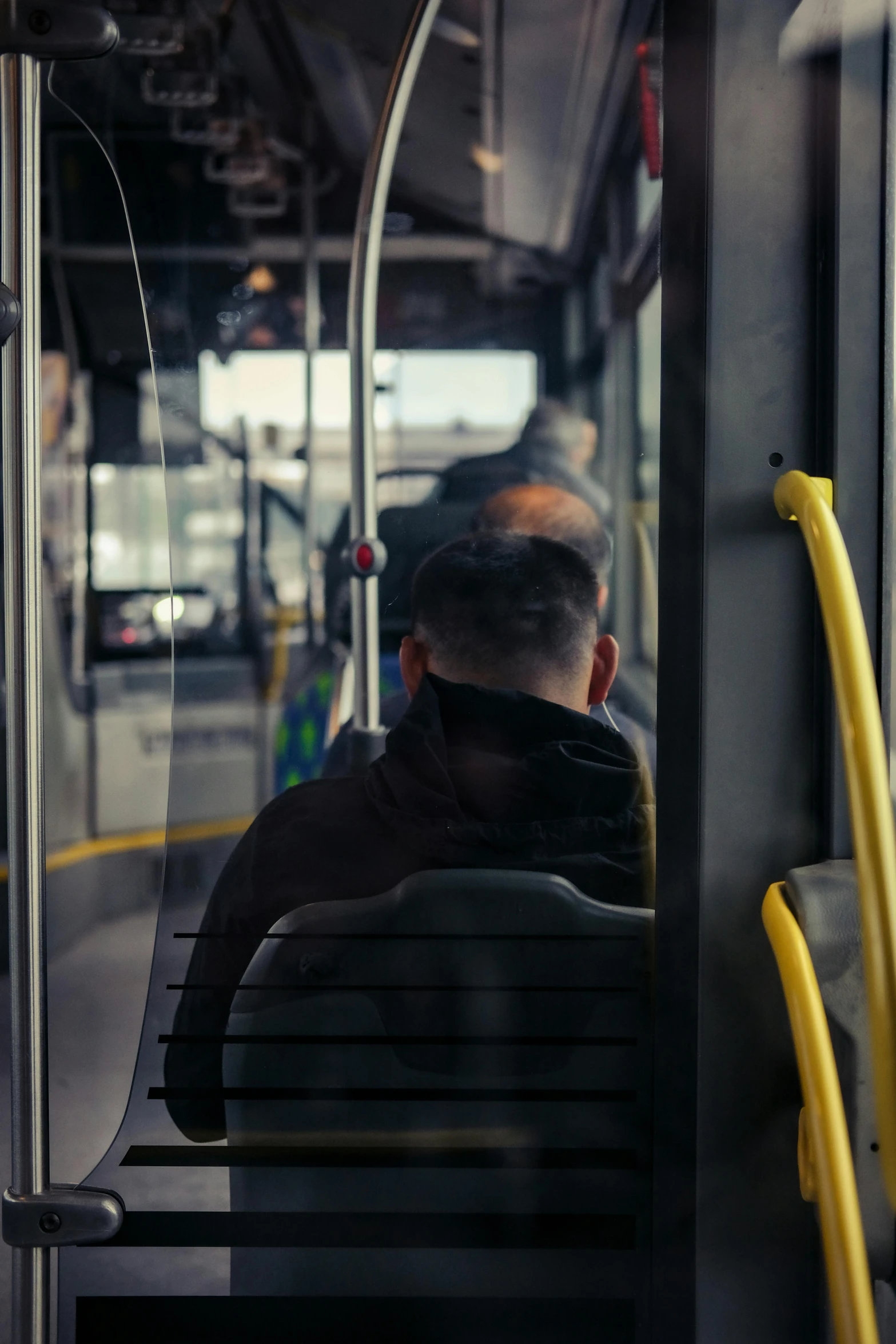 a man sitting on a bus looking out the window, back facing the camera, square, slightly pixelated, helmet is off