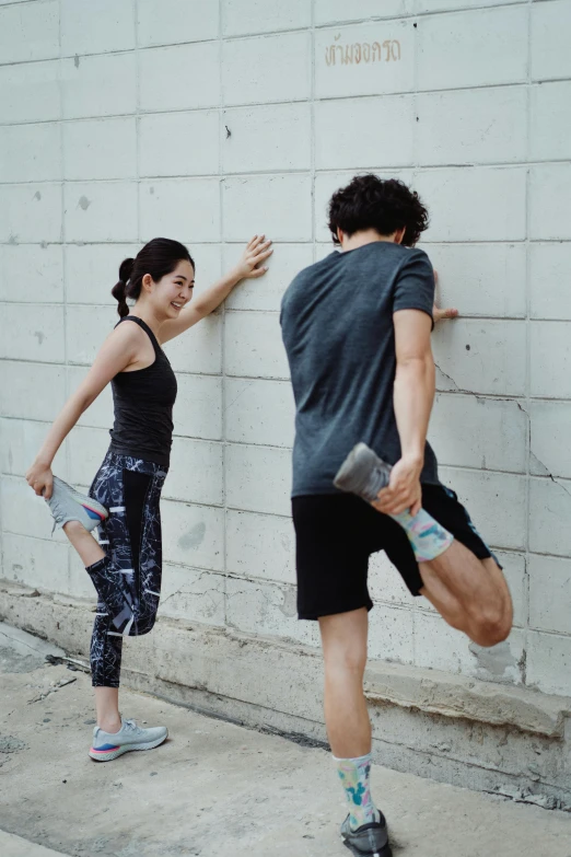 a man and a woman standing next to a wall, by Jang Seung-eop, pexels contest winner, doing splits and stretching, profile image, working out, pointing