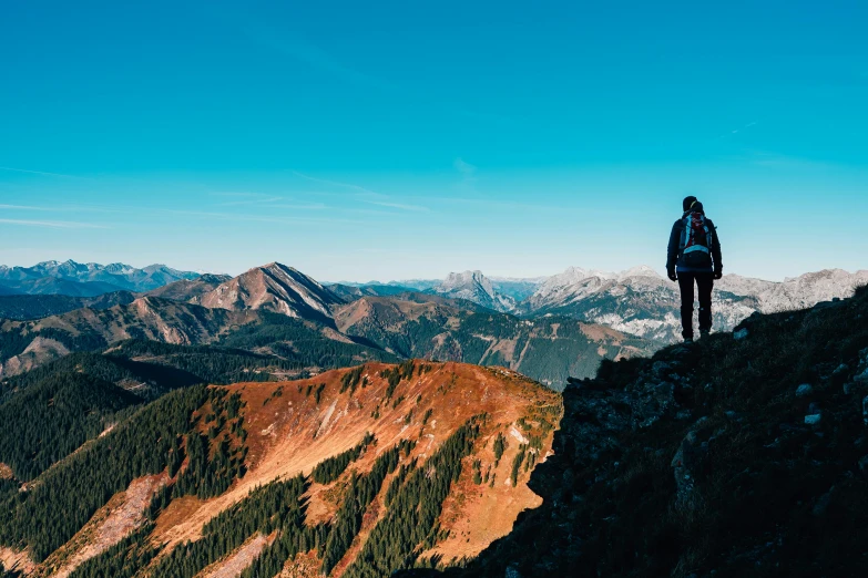 a person standing on top of a mountain, by Niko Henrichon, pexels contest winner, clear blue skies, fall season, thumbnail, multiple stories