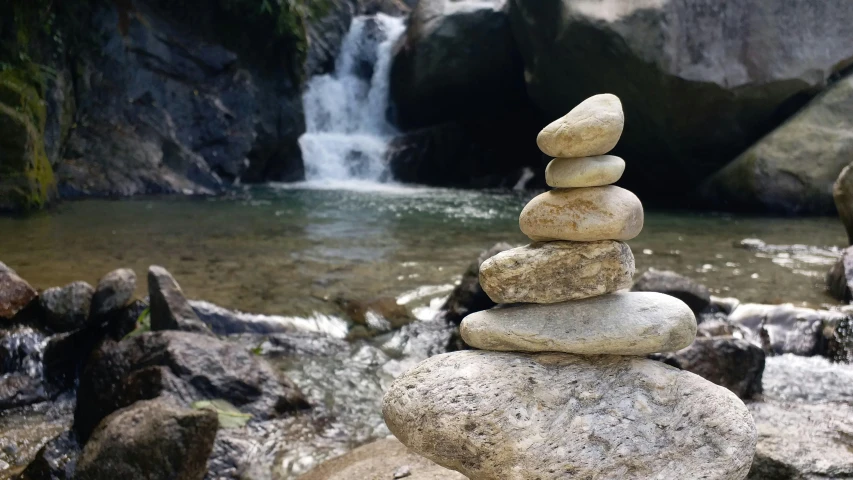 a pile of rocks sitting in front of a waterfall, inspired by Shūbun Tenshō, unsplash, land art, las pozas, beside the river, 2 0 0 0's photo, nepal