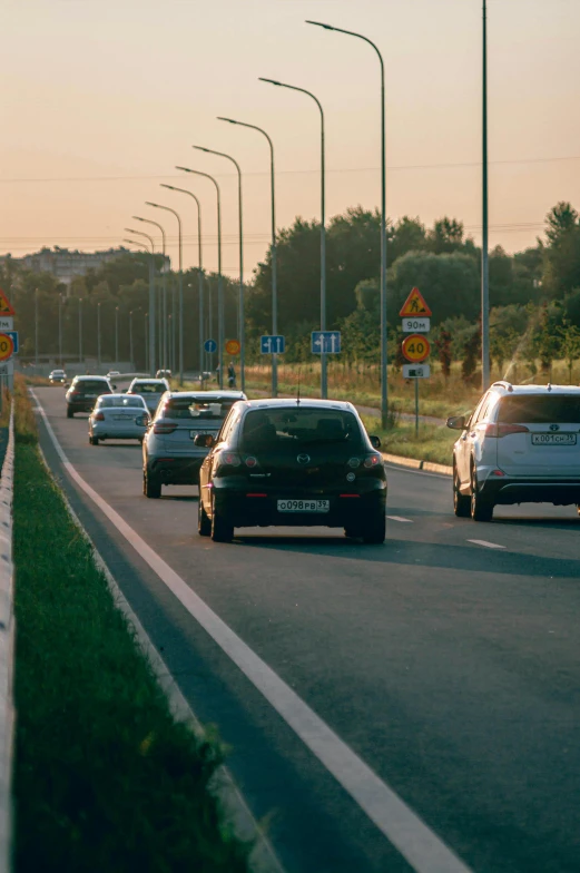 a group of cars driving down a highway, by Adam Marczyński, evening sunlight, square, low quality photo, traffic signs