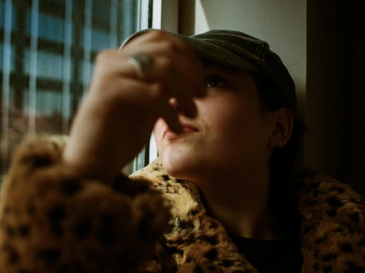 a woman in a leopard coat looking out a window, inspired by Elsa Bleda, pexels contest winner, hand on his cheek, joey king, she is wearing a hat, directional sunlight skewed shot