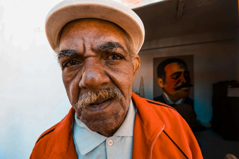 a close up of a person wearing a hat, a portrait, by William Berra, pexels contest winner, long and orange mustache, cuban setting, tight wrinkled cloath, markings on his face