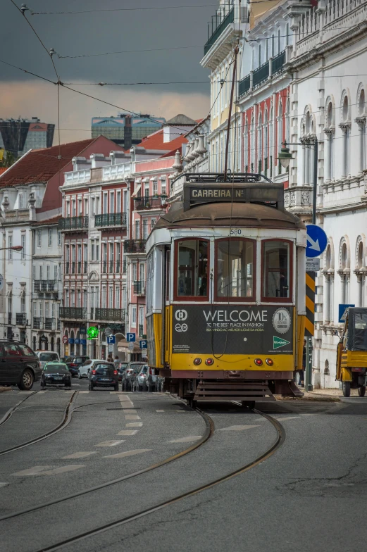 a yellow trolley traveling down a street next to tall buildings, inspired by Almada Negreiros, pexels contest winner, happening, baroque winding cobbled streets, square, brown, metro
