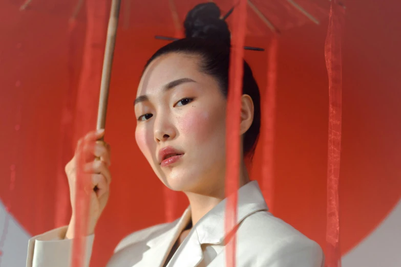 an asian woman with a red umbrella looks out through the curtain