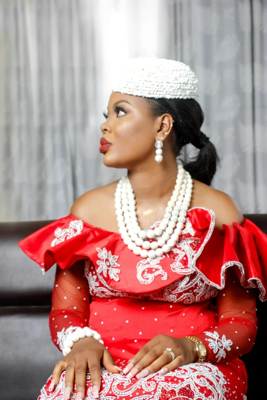 a woman in a red dress sitting on a couch, by Chinwe Chukwuogo-Roy, pexels, white regal gown, real pearls, wearing traditional garb, glamor pose