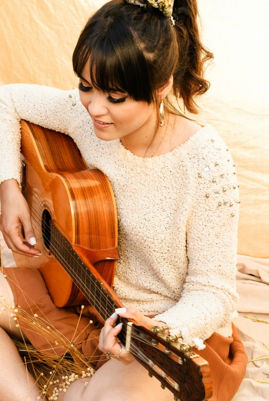 a woman sitting on the ground playing a guitar, chloe bennet, ethereal details, sweater, al fresco