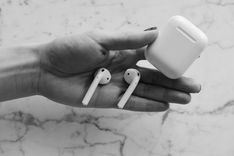 a person holding a pair of airpods in their hand, a black and white photo, by Emma Andijewska, pexels, hyper - realistic, square, apples, bone