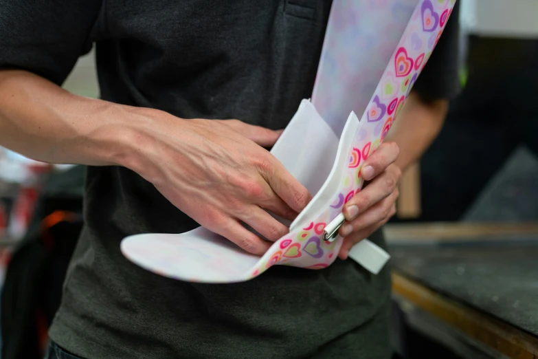 a close up of a person holding a piece of paper, a silk screen, wearing knee and elbow pads, full colour, small manufacture, paisley