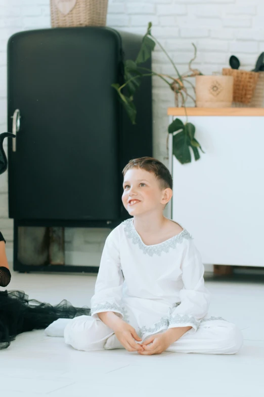 a little boy sitting on the floor next to a woman, a character portrait, pexels contest winner, light and space, wearing a white folkdrakt dress, 15081959 21121991 01012000 4k, in a white boho style studio, a still of a happy