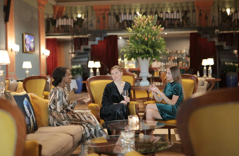 a group of women sitting in a living room next to each other, pexels, renaissance, paris hotel style, with a drink, profile image, amanda lilleston