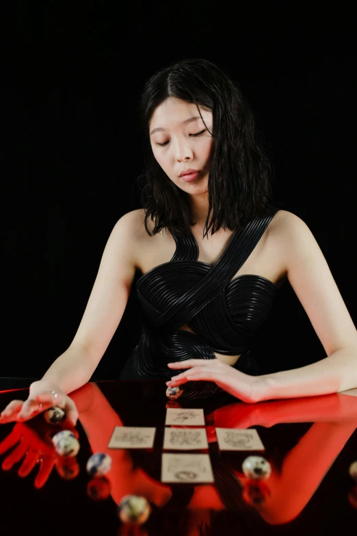 a woman in a black dress playing cards on a table, an album cover, inspired by Ma Lin, kinetic art, spell casting wizard, live performance, gongbi, looks a blend of grimes