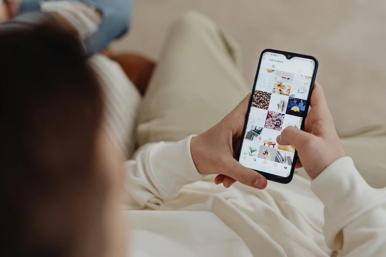 a person sitting on a couch holding a cell phone, a picture, by Julia Pishtar, trending on pexels, on my bed, 9 9 designs, instagram post, everything fits on the screen