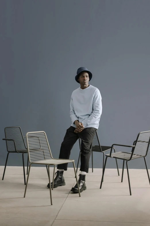 a man sitting on a chair in a room, grey and blue theme, official store photo, black man, utilitarian