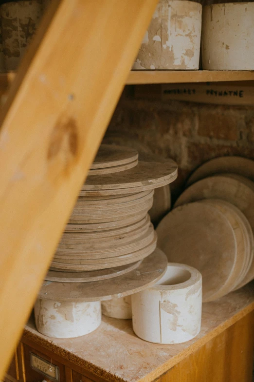 a stack of plates sitting on top of a wooden shelf, inside a shed, sandstone, various sizes, 300mm