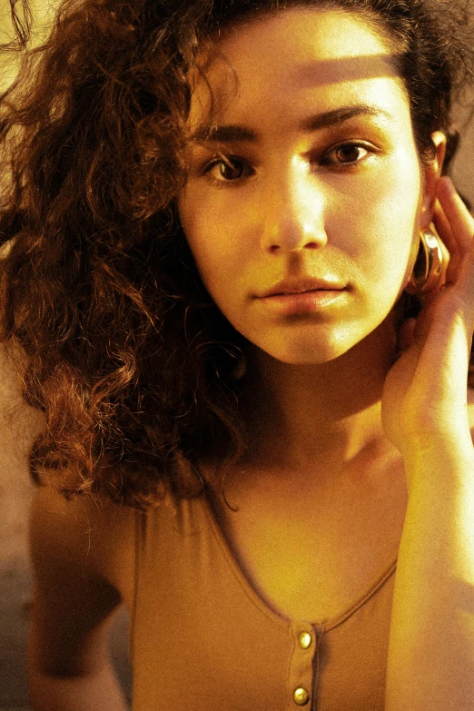 a woman holding a cell phone to her ear, an album cover, inspired by Nan Goldin, photorealism, brown curly hair, bathed in golden light, serious look, loosely cropped