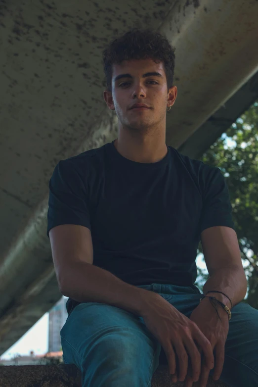 a young man sitting on a ledge under a bridge, an album cover, inspired by John Luke, pexels contest winner, realism, wearing tight shirt, headshot profile picture, grainy low quality, asher duran