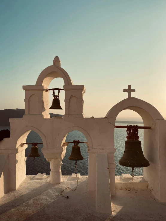 a group of bells hanging from the side of a building, a picture, pexels contest winner, neoclassicism, next to the sea, holy glow, white marble interior photograph, brown