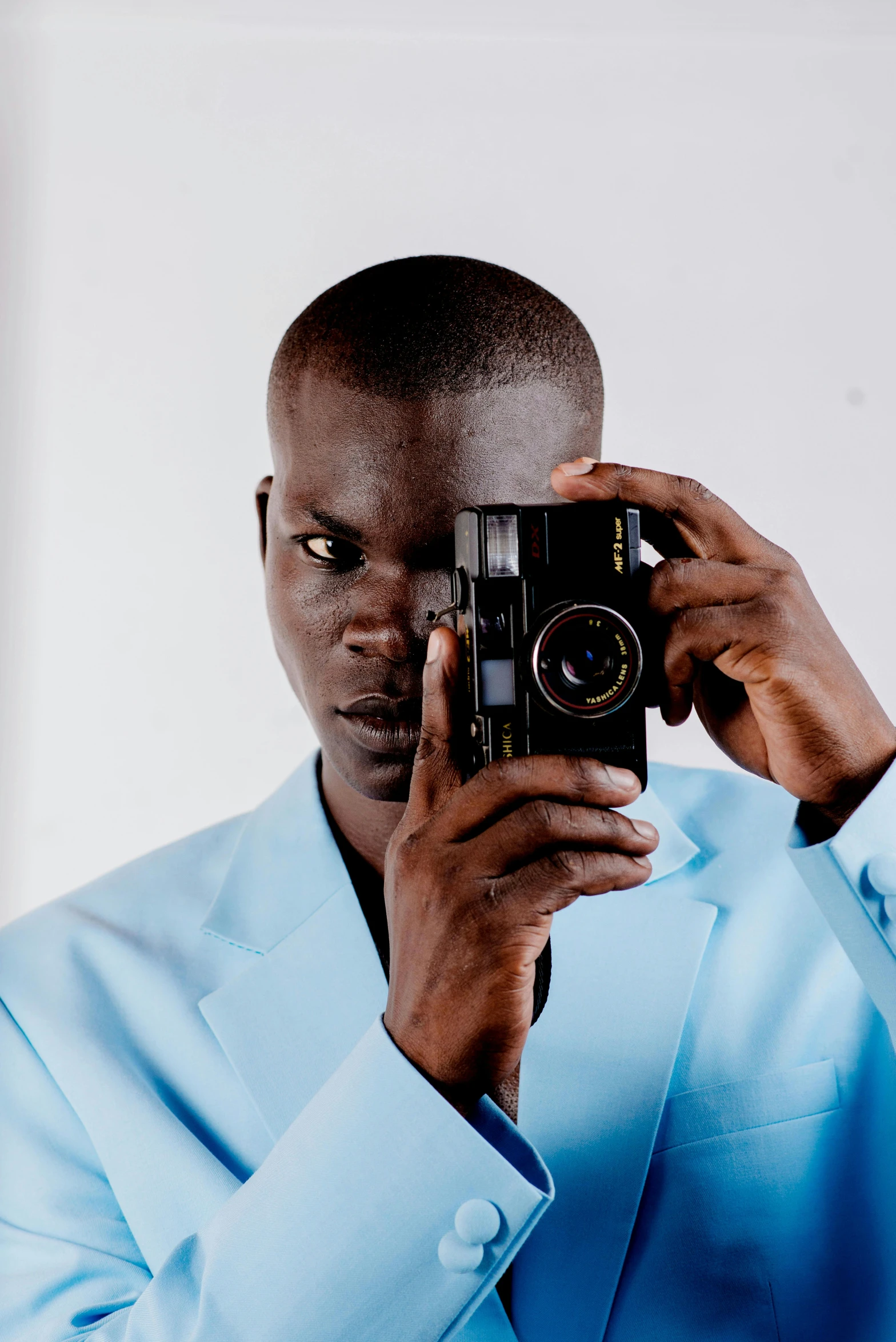 a man taking a picture with a camera, by Dean Ellis, adut akech, wearing a light blue suit, looking intensely at the camera, in colour