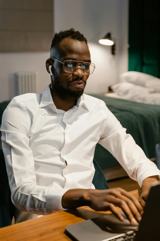 a man sitting in front of a laptop computer, by Cosmo Alexander, trending on pexels, renaissance, wearing a white button up shirt, african man, nerdy, someone sits in bed