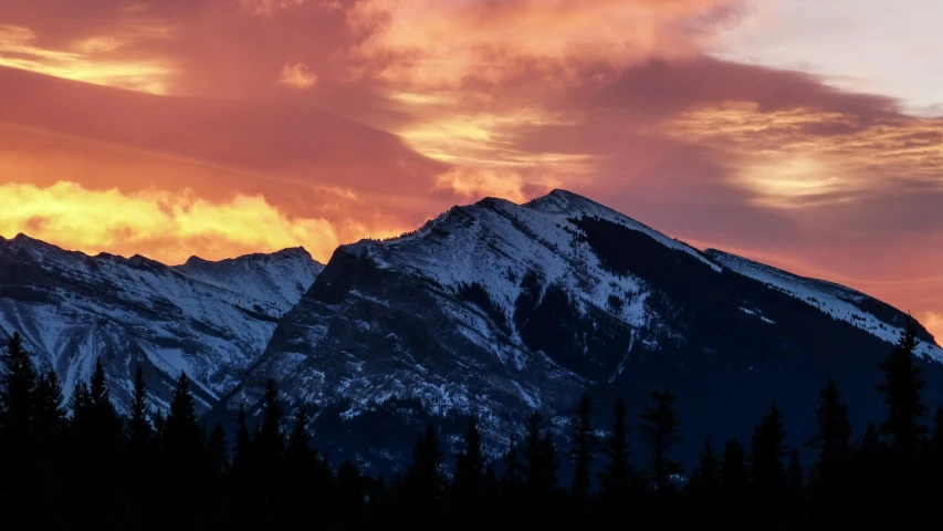 the sun is rising above the mountains as clouds hovers above