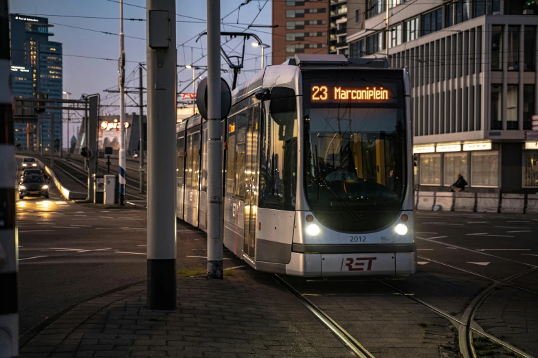 a train traveling down a city street next to tall buildings, a picture, by Jan Tengnagel, pexels contest winner, happening, bus station, delft, light tan, street tram