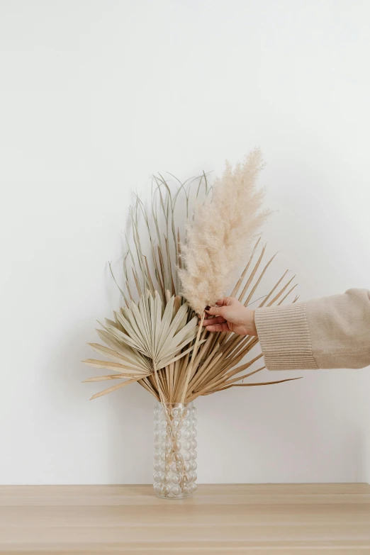 two people hold some brown grass next to a vase