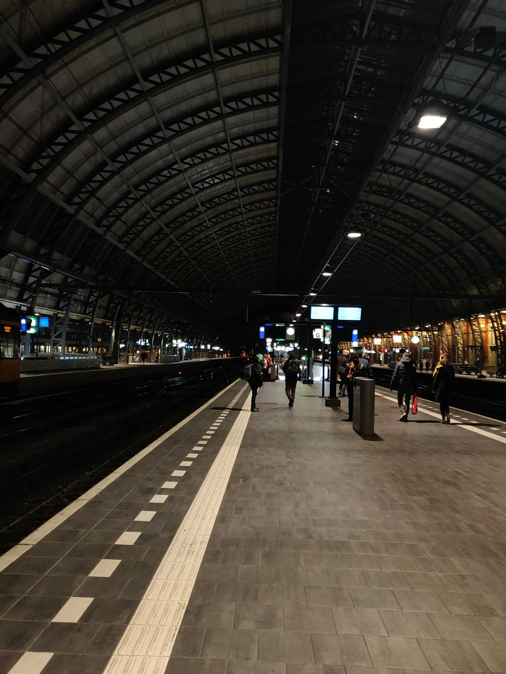 people walking across a train station platform at night
