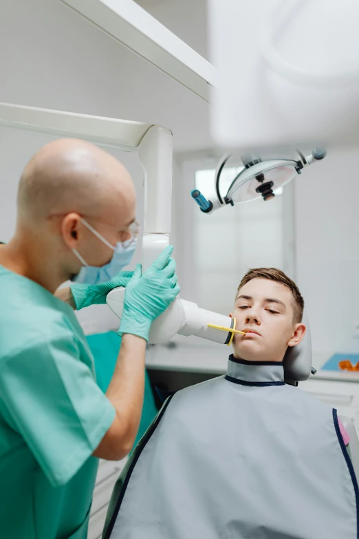 a man getting his teeth examined by a dentist, a colorized photo, by Adam Marczyński, pexels contest winner, square masculine jaw, surgical iv drip, gold, where a large